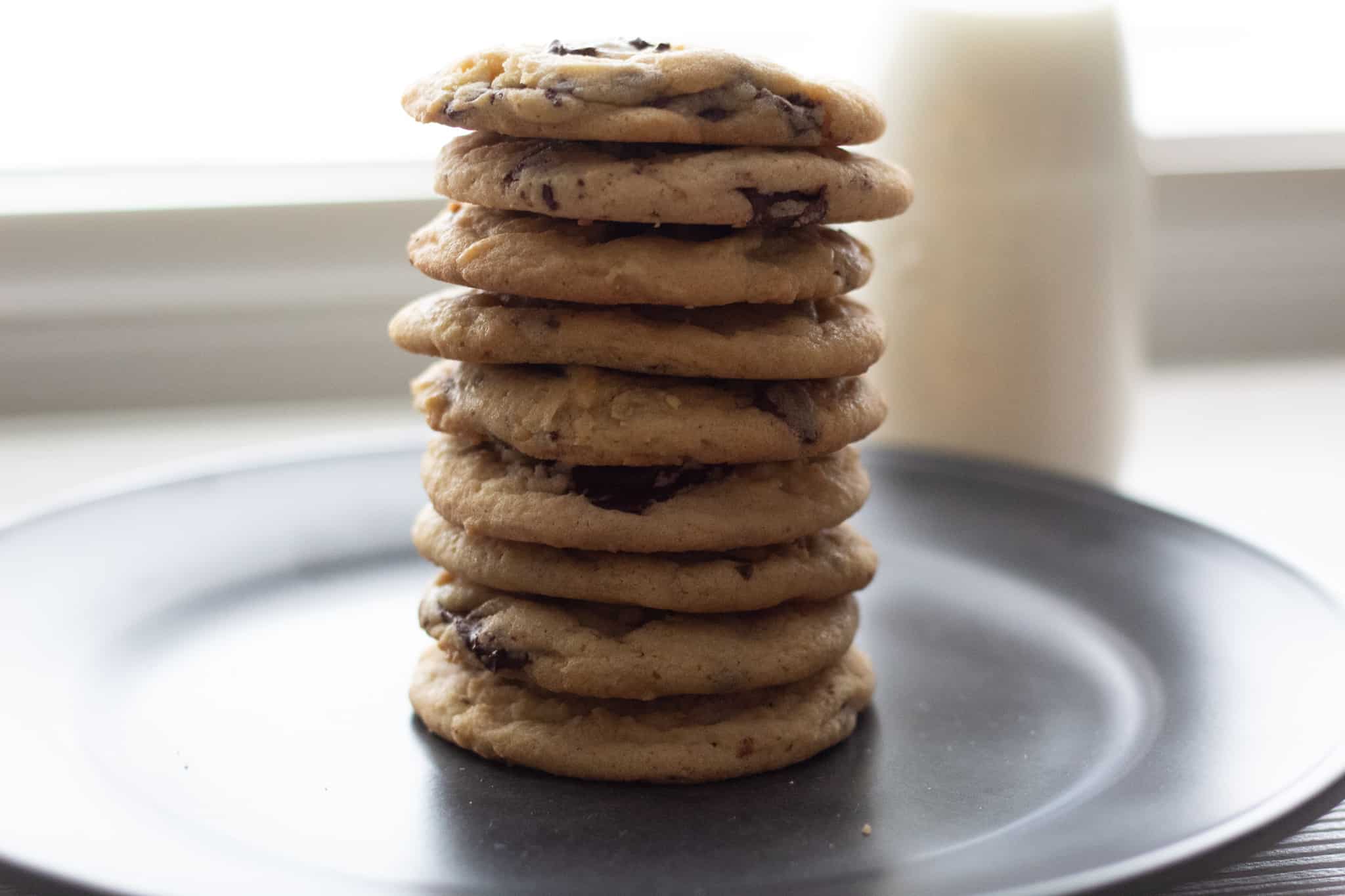 Stack of chocolate chunk cookies on a dark plate with milk in the background