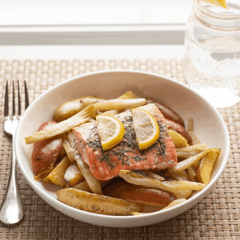 Plate of lemon topped salmon on roasted fennel and potatoes with a glass of water