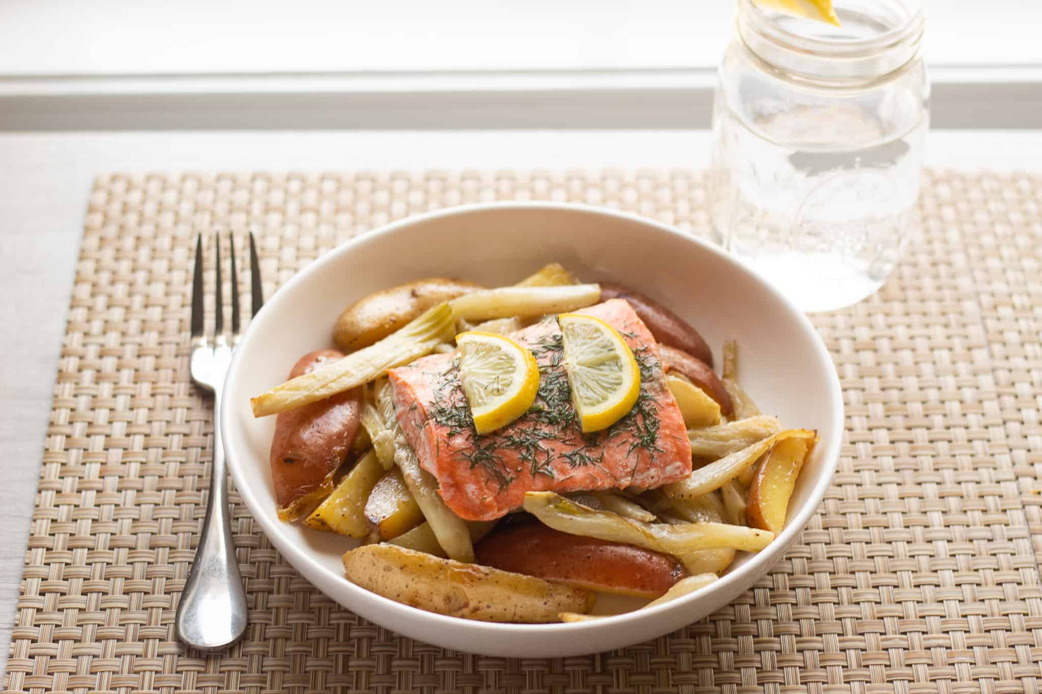 Plate of lemon topped salmon sitting on top of roasted fennel and potatoes.