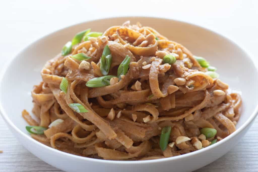 Up close image of peanut noodles topped with green onions and chopped peanuts.