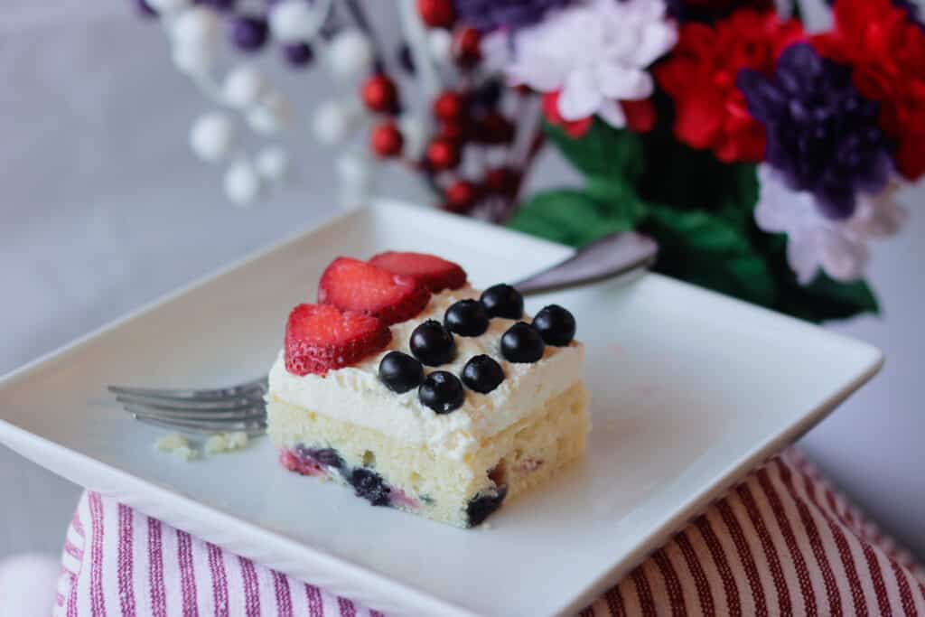 Slice of frosted cake with strawberries and blueberries on top