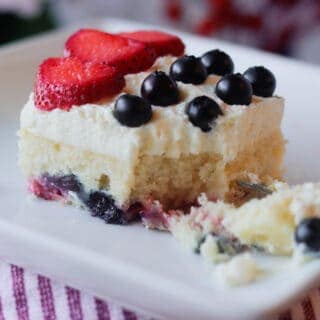 Slice of mixed berry sheet cake with whipped mascarpone frosting, topped with strawberries and blueberries