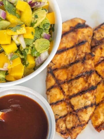 Grilled bbq chicken with a bowl of mango avocado salsa and bowl of bbq sauce