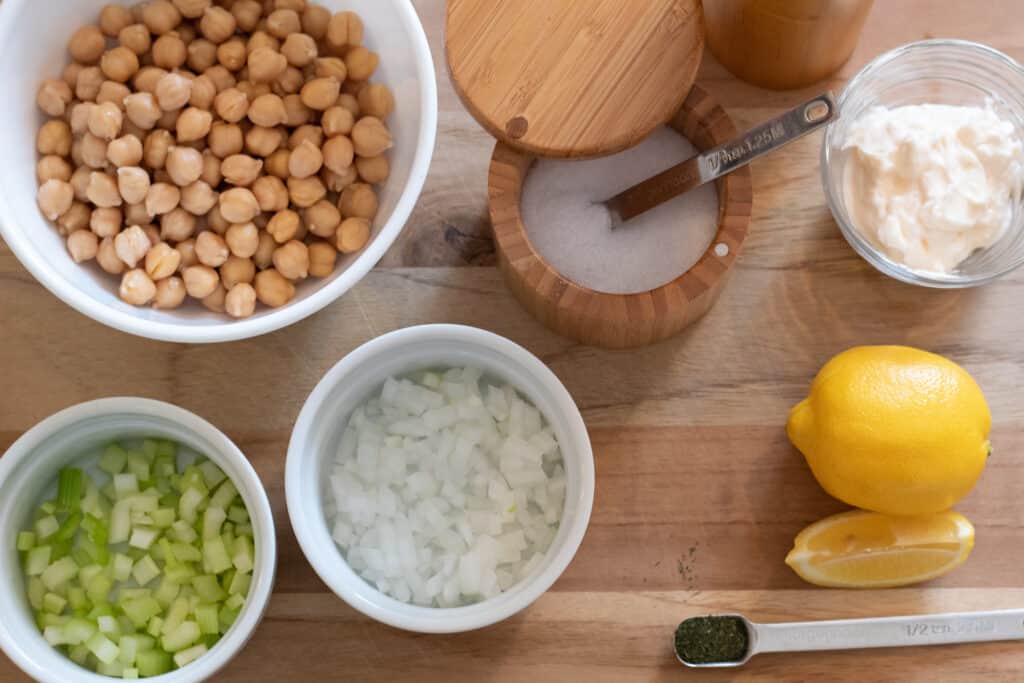 Chickpea salad ingredients including chickpeas, mayo, diced celery and onion, lemon, dill, and salt.
