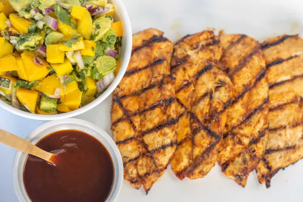 Grilled chicken breasts with a bowl of mango avocado salsa and a bowl of bbq sauce