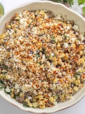 Bowl of Mexican Street Corn Salad with cilantro and lime wedges