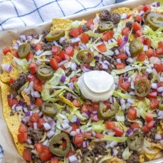 Tray of beef nachos with lettuce, tomatoes, red onion, jalapenos, and sour cream