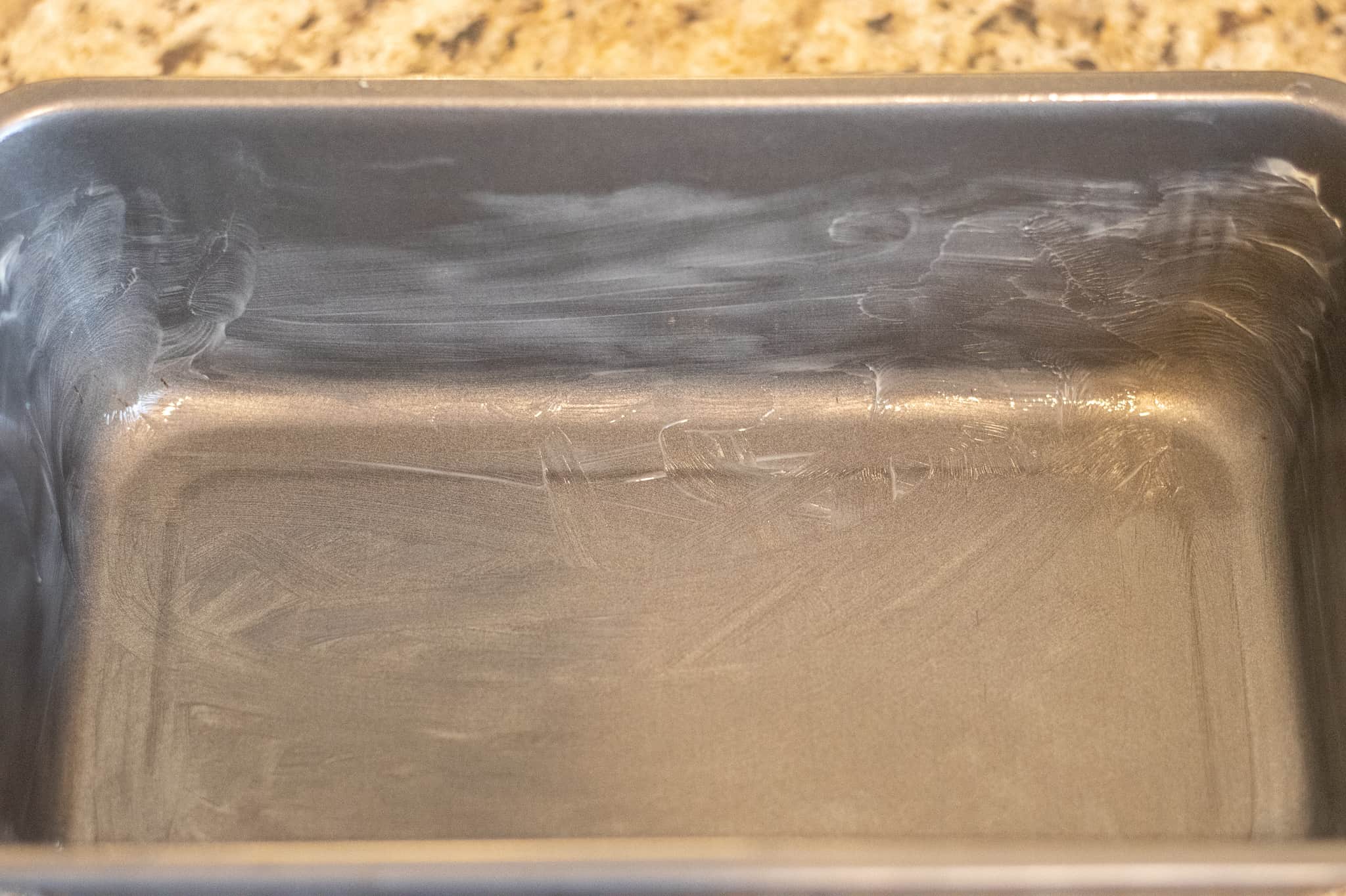 A metal loaf pan greased with a layer of butter.