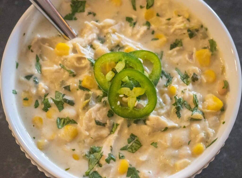 Creamy white chicken chili in a white bowl topped with extra cilantro and three slices of jalapeno