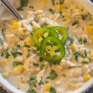 Creamy white chicken chili in a white bowl topped with extra cilantro and three slices of jalapeno
