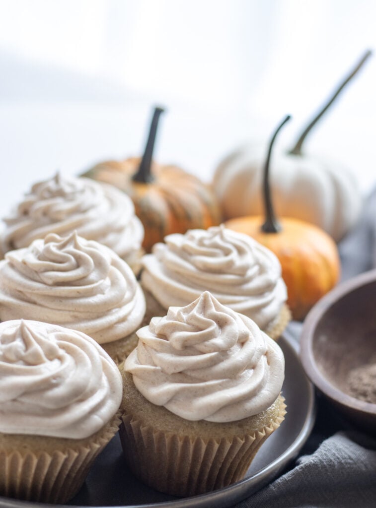Cupcakes next to a wooden bowl with spices and pumpkins in the background
