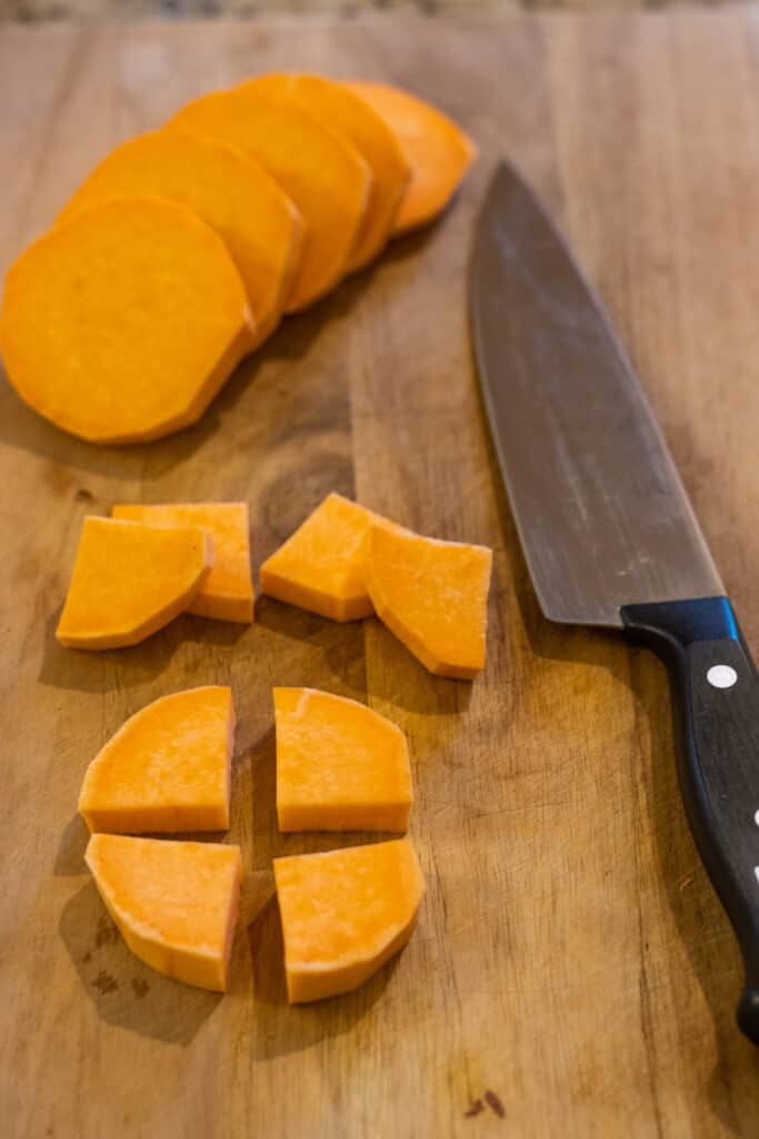 Peeled sweet potato sliced then quartered next to a chef's knife.