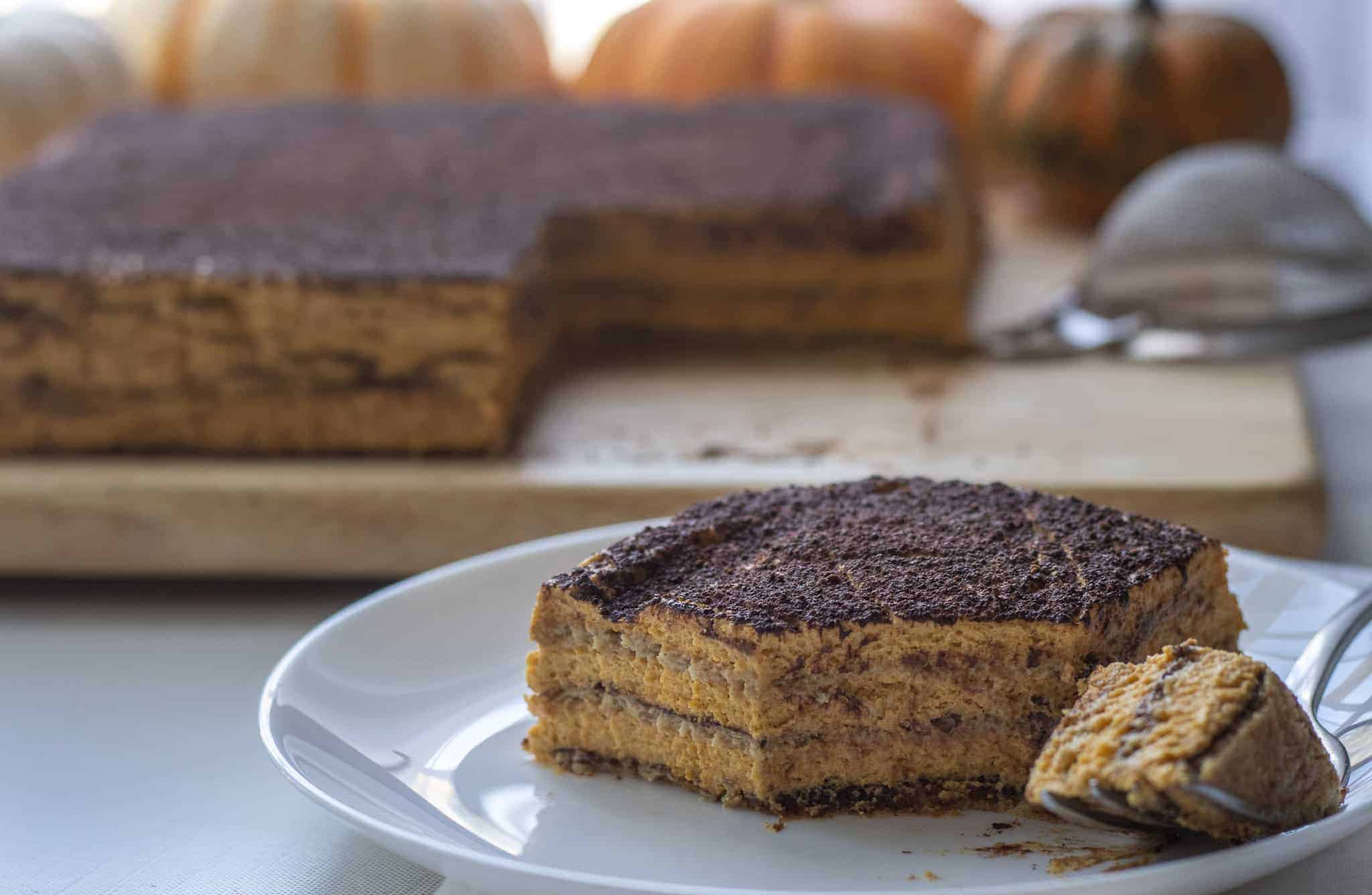 Slice of pumpkin icebox cake with a forkful next to it and the cake in the background with pumpkins