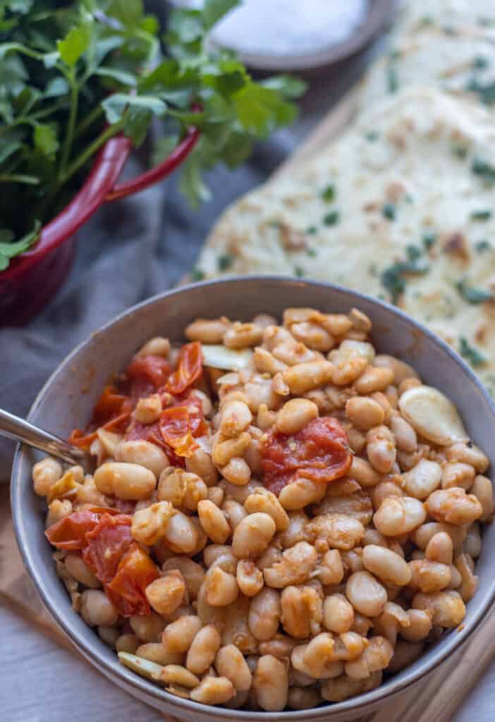 Bowl of white beans with burst tomatoes next to flatbreads and parsley