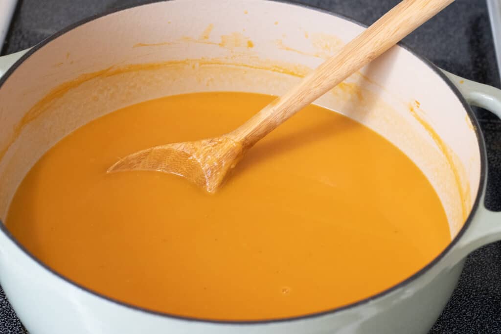 Roasted creamy pumpkin and coconut soup in a Dutch oven with a wooden spoon