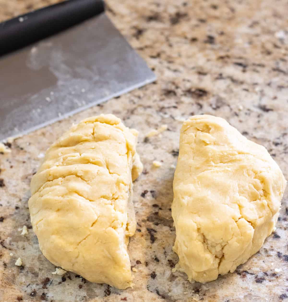 Pie crust dough cut in half with a bench cutter in the back.