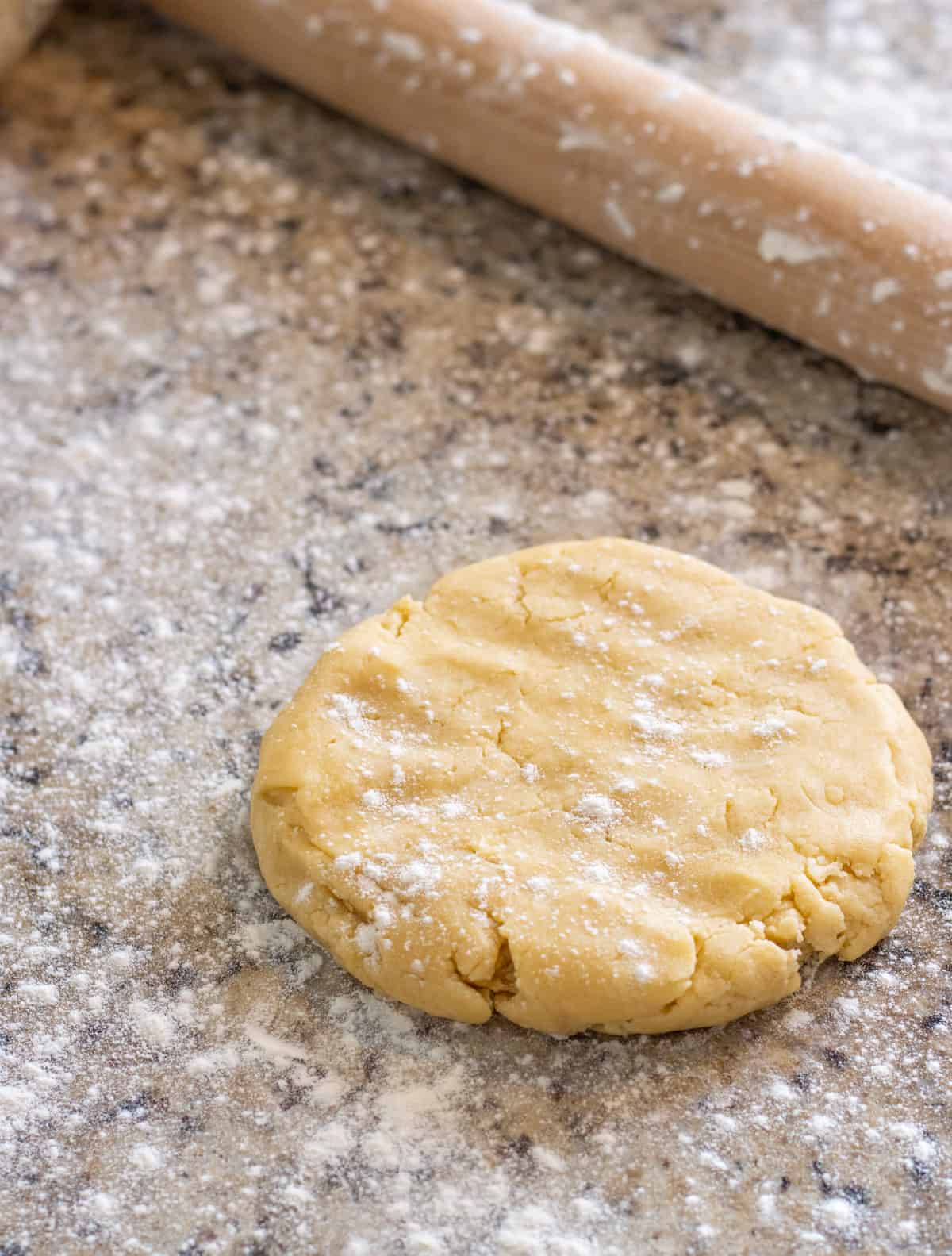 Round pie crust dough on a counter with a rolling pin all sprinkled with flour.