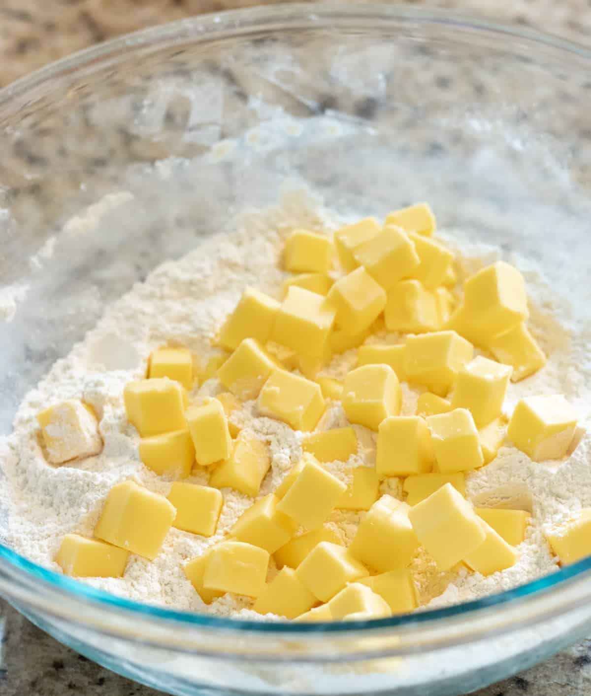 Butter cubes on top of flour in a glass bowl.