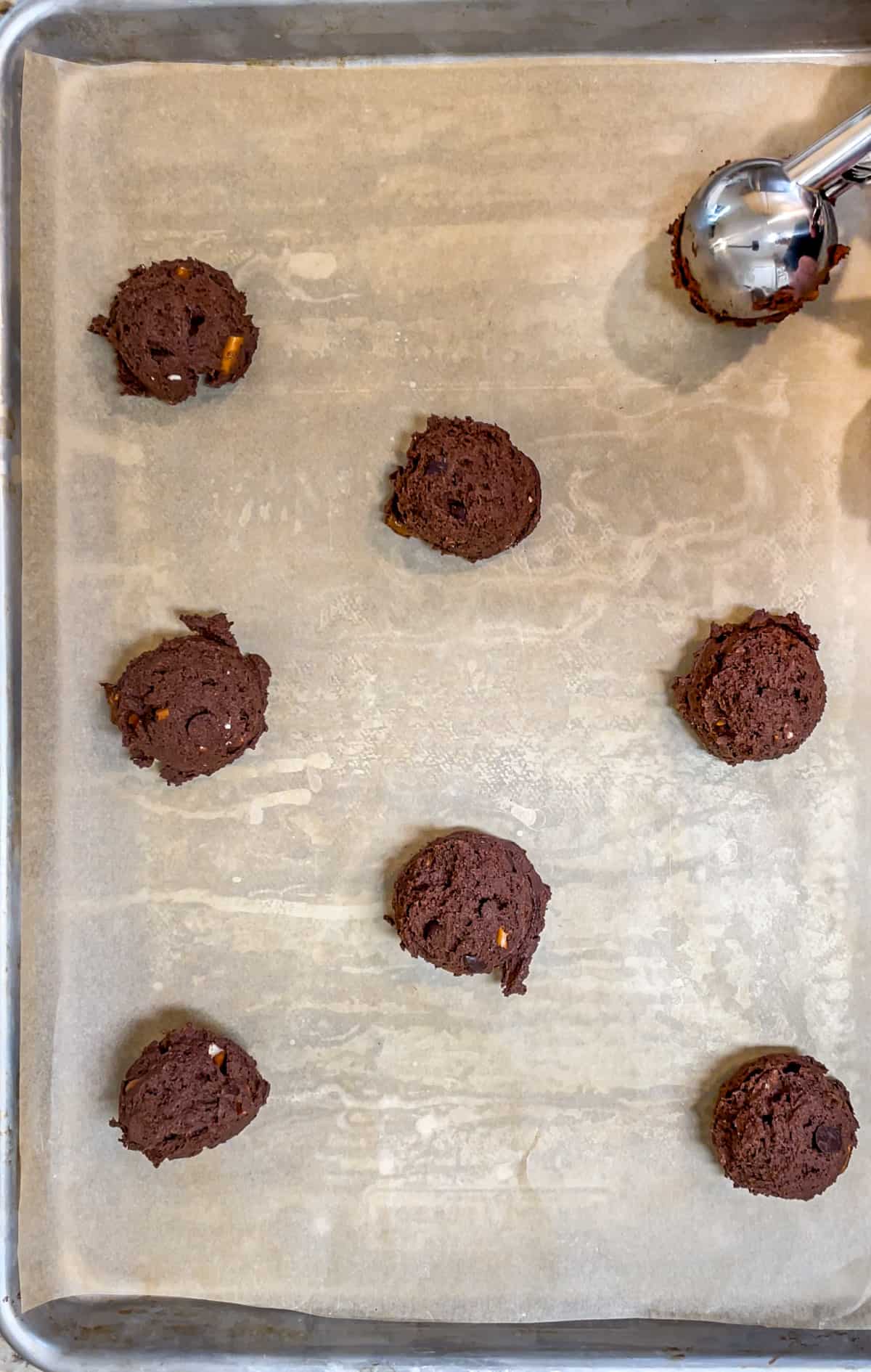 Chocolate cookie dough balls on a parchment lined baking sheet ready for the oven.