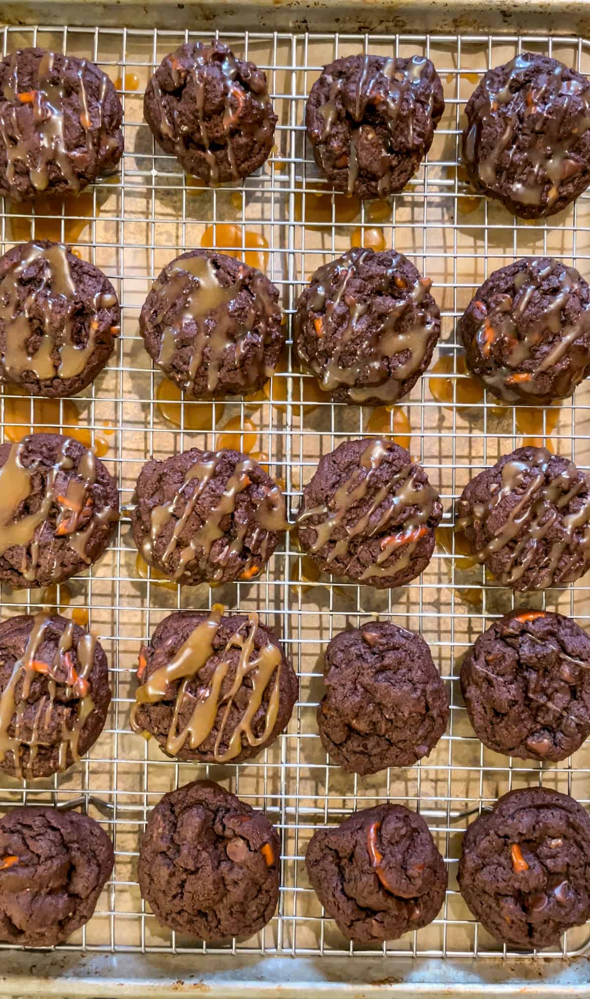 Chocolate pretzel cookies on a wire rack being drizzled with caramel sauce.