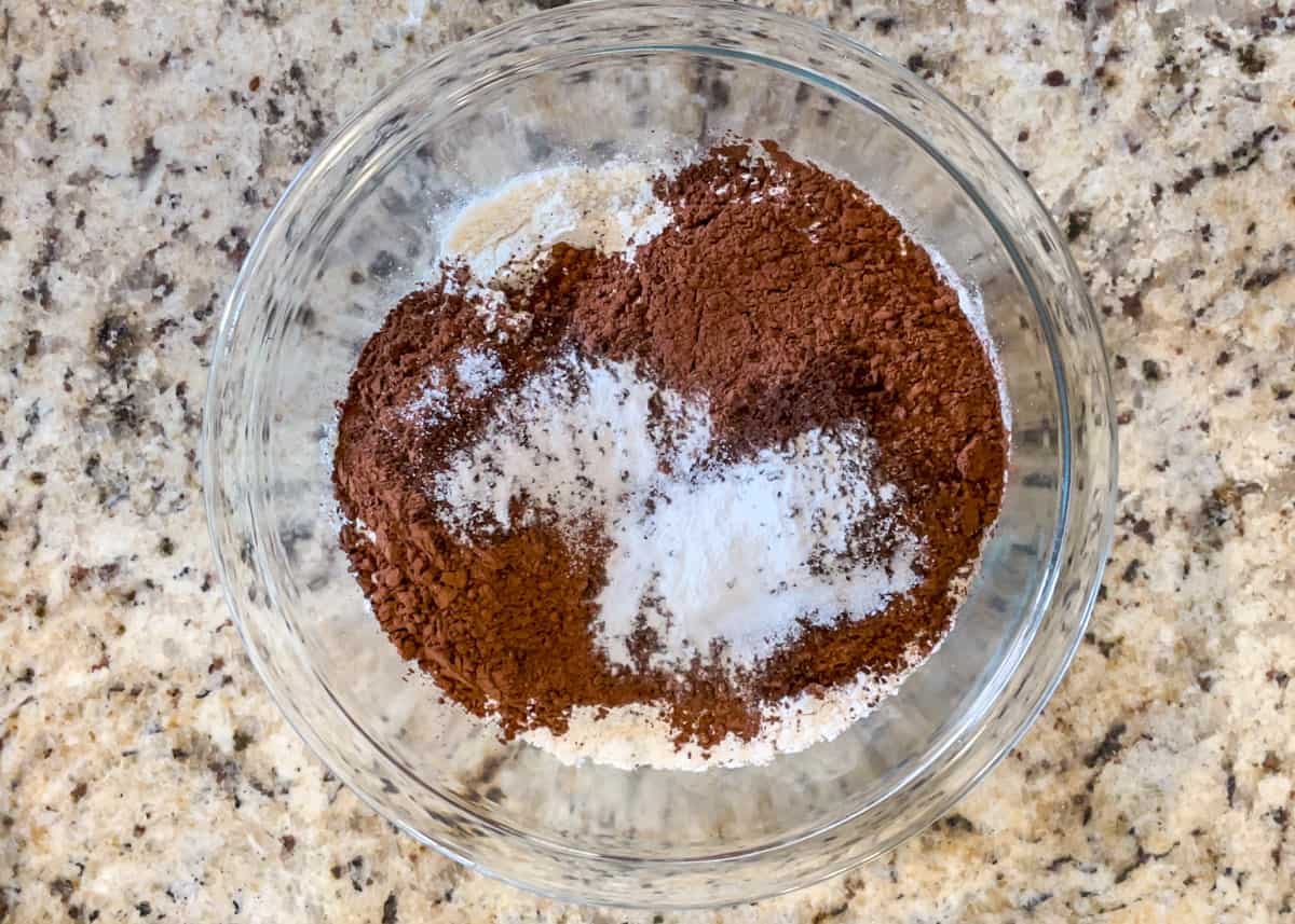 Glass bowl with flour, cocoa powder, espresso powder, baking soda, and salt ready to be mixed together.