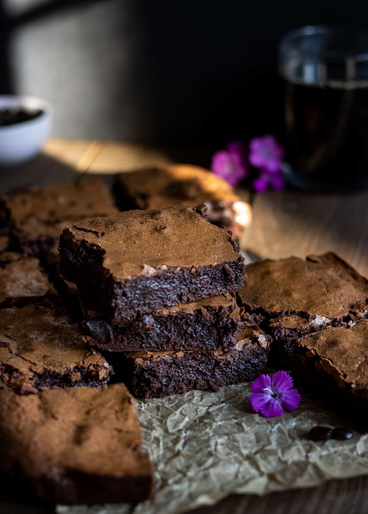 Brownies stacked up with a cup of coffee and flowers in the background.