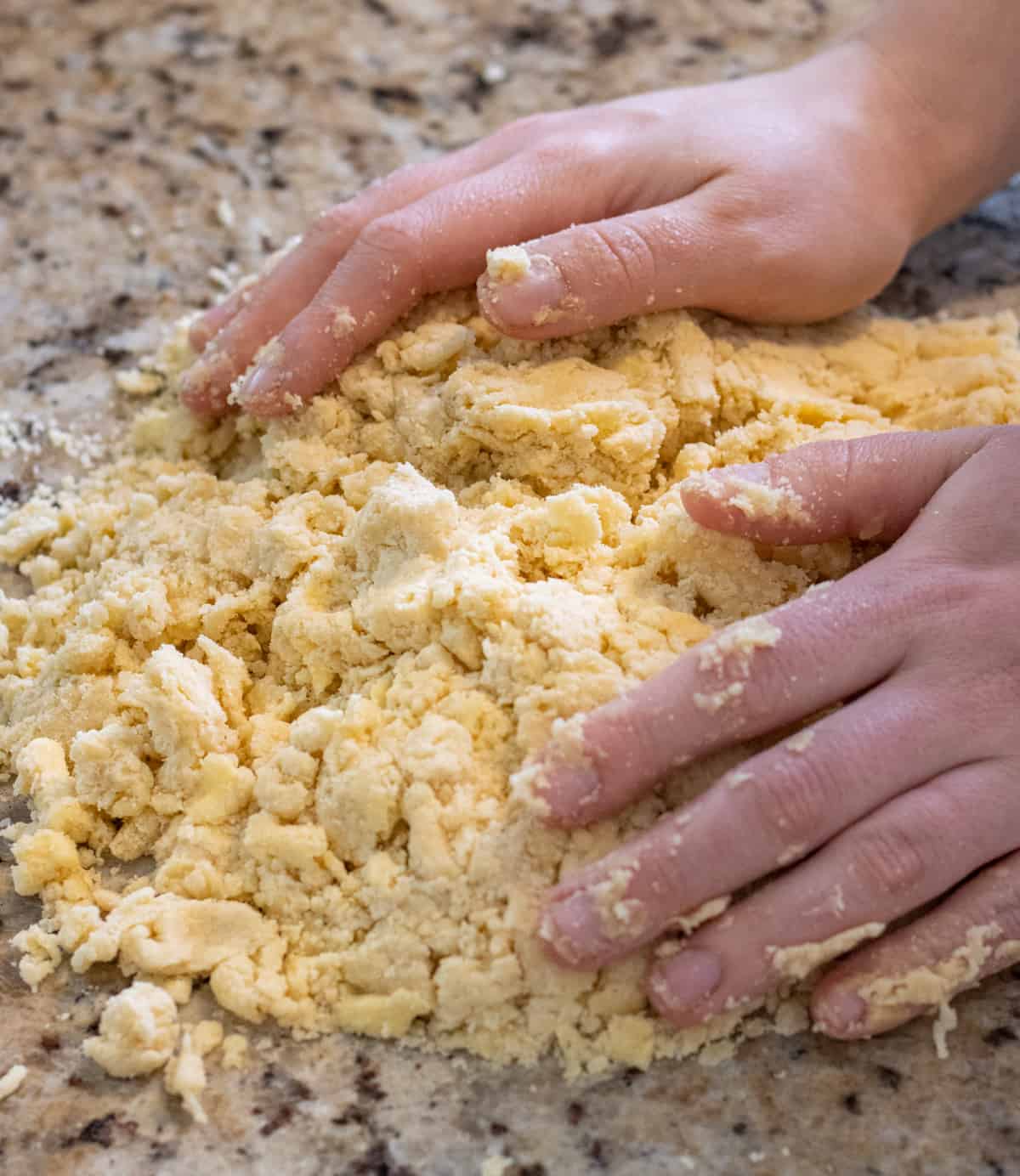 Pie crust dough on the counter being pressed together by two hands.