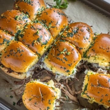 French dip sliders on a board with au jus and parsley.