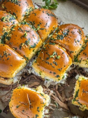 French dip sliders on a board with au jus and parsley.