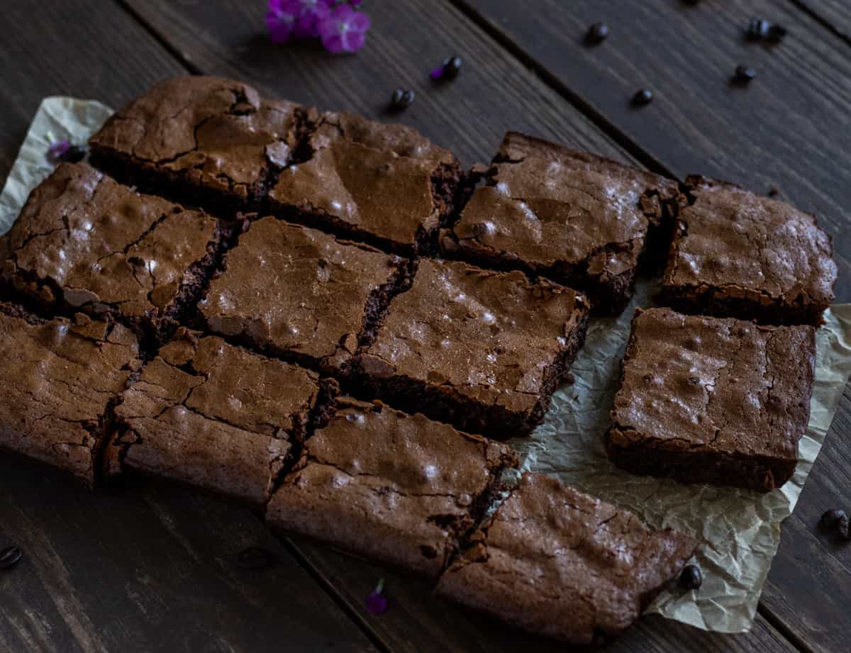 Espresso brownies on parchment paper on a dark board with purple flowers and coffee beans. 