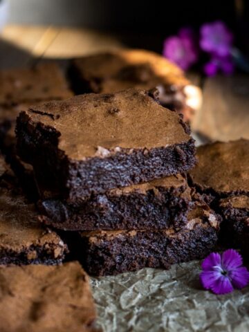 Brownies stacked on top of each other on a dark board with purple flowers.