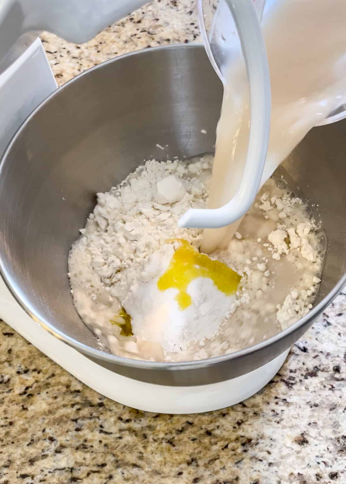 Yeast water being poured into a mixing bowl with flour, sugar, salt, and melted butter.