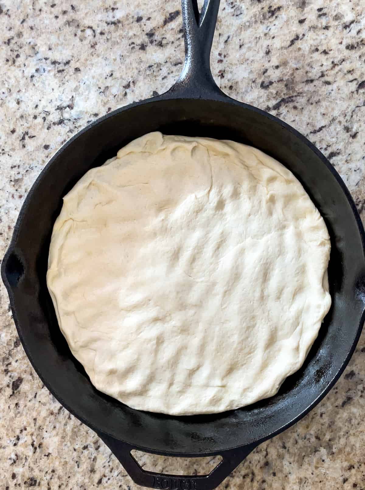 Pizza dough spread out in the bottom of a cast iron pan.