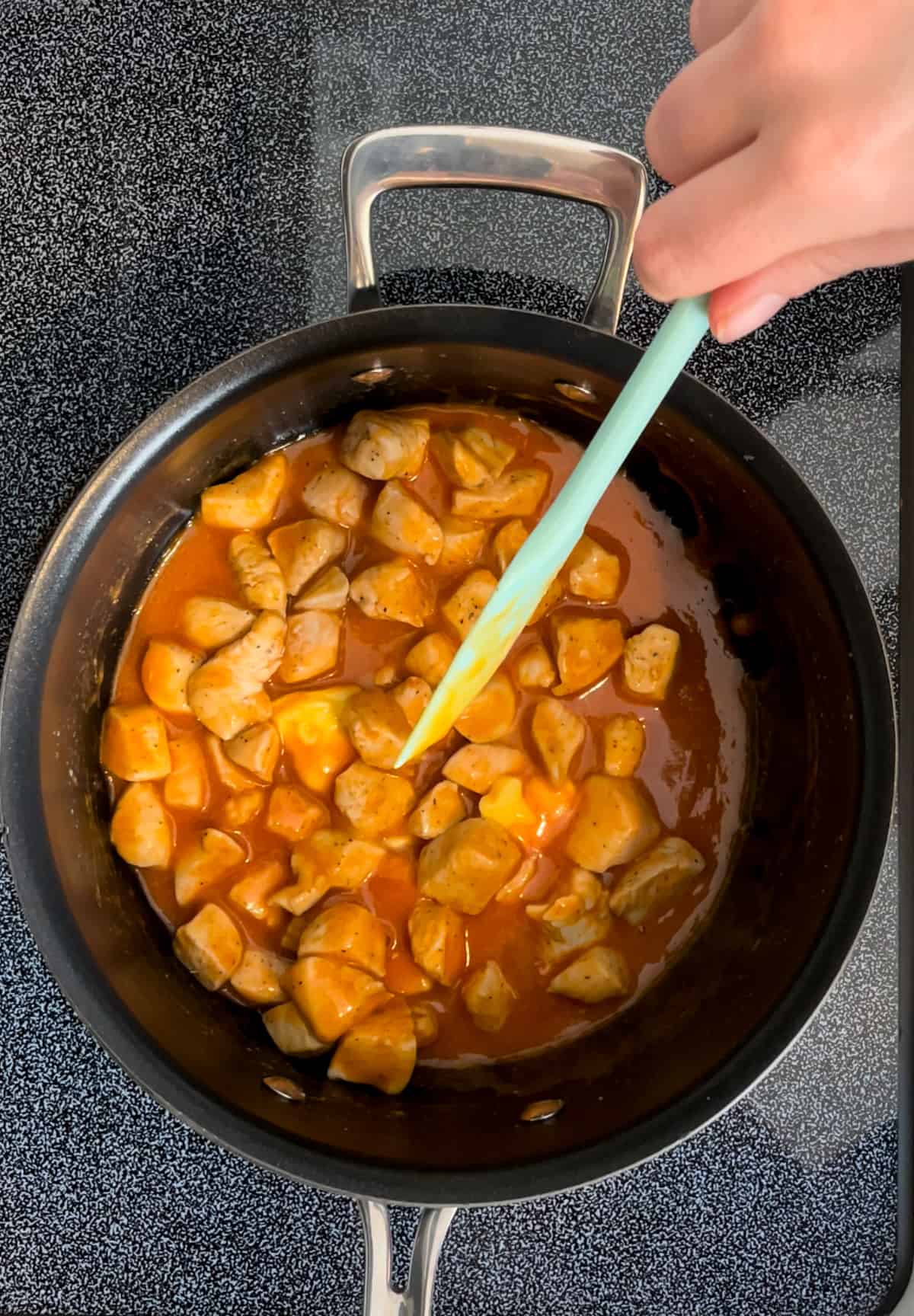 Diced chicken cooking in a pot with buffalo sauce.