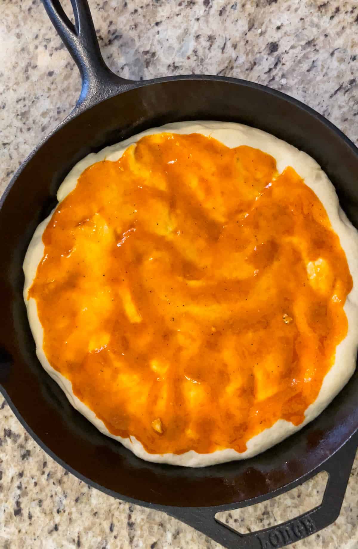 Buffalo sauce on a pizza crust in a cast iron pan.
