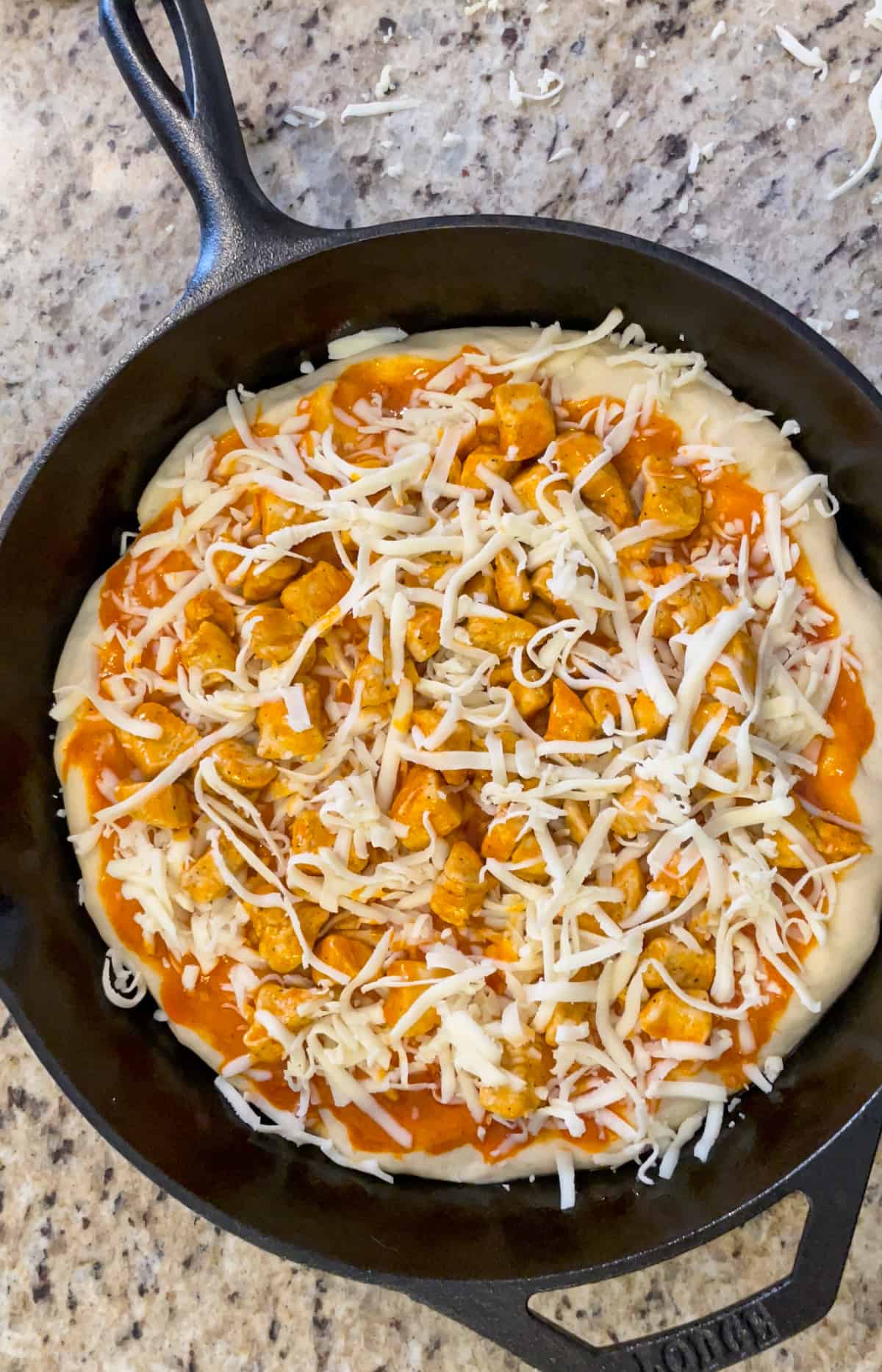 Buffalo chicken pizza assembled in a cast iron pan and ready for the oven.