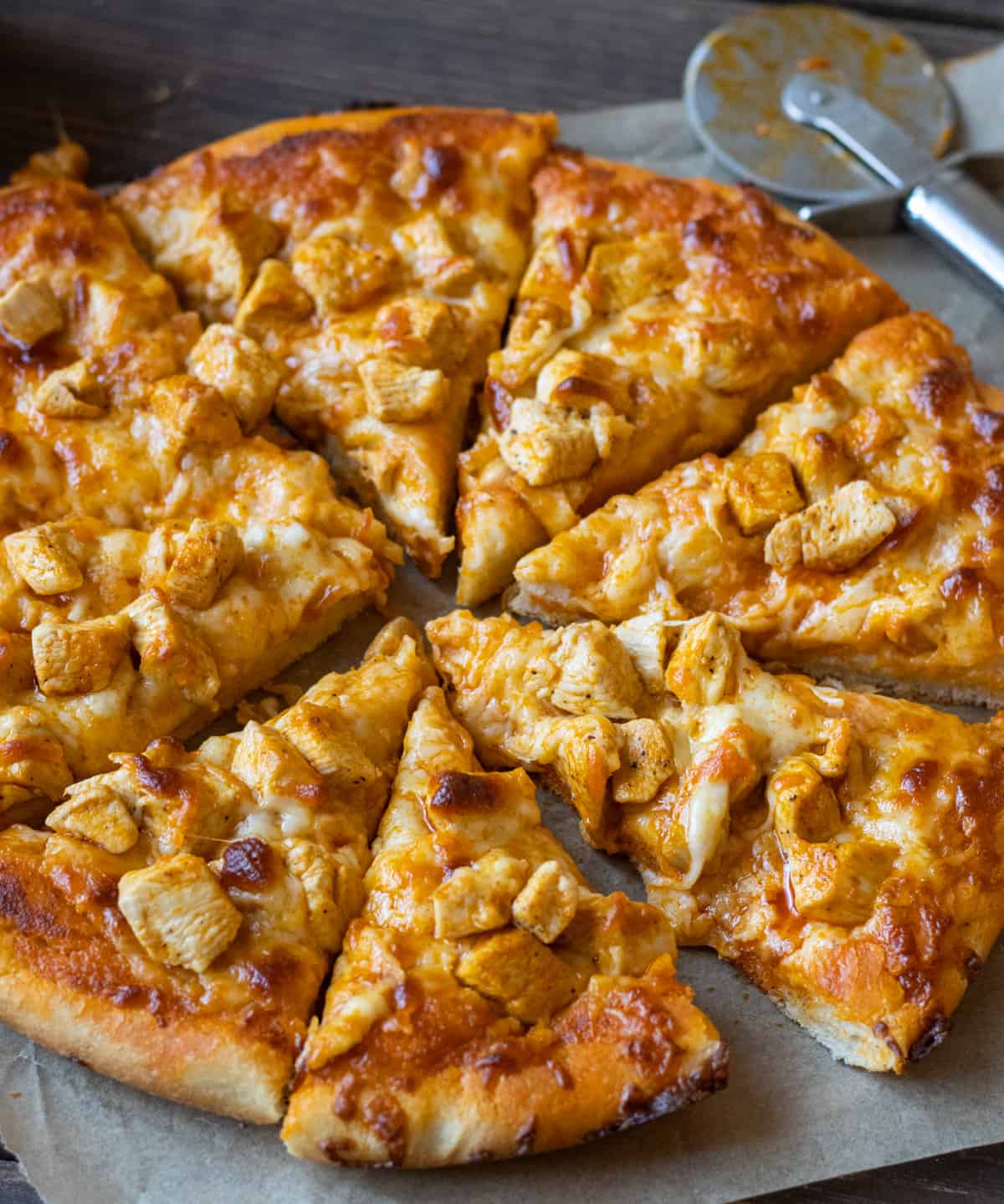 Buffalo Chicken Pizza cut into slices on parchment paper with a pizza cutter in the background.