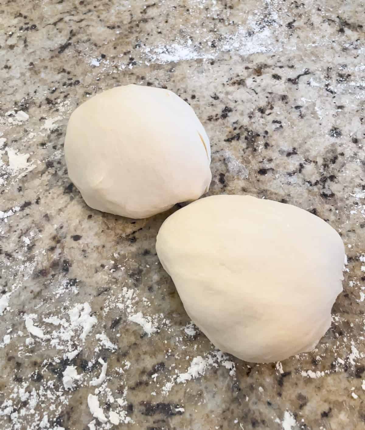 Two pizza dough balls on a lightly floured counter.