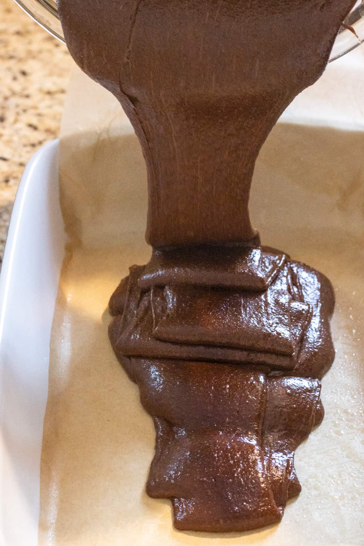 Espresso brownie batter being poured into a parchment lined baking dish.