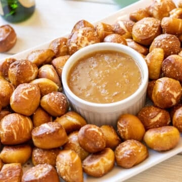 Pretzel bites on a platter with honey mustard dip and a green bottle in the background.
