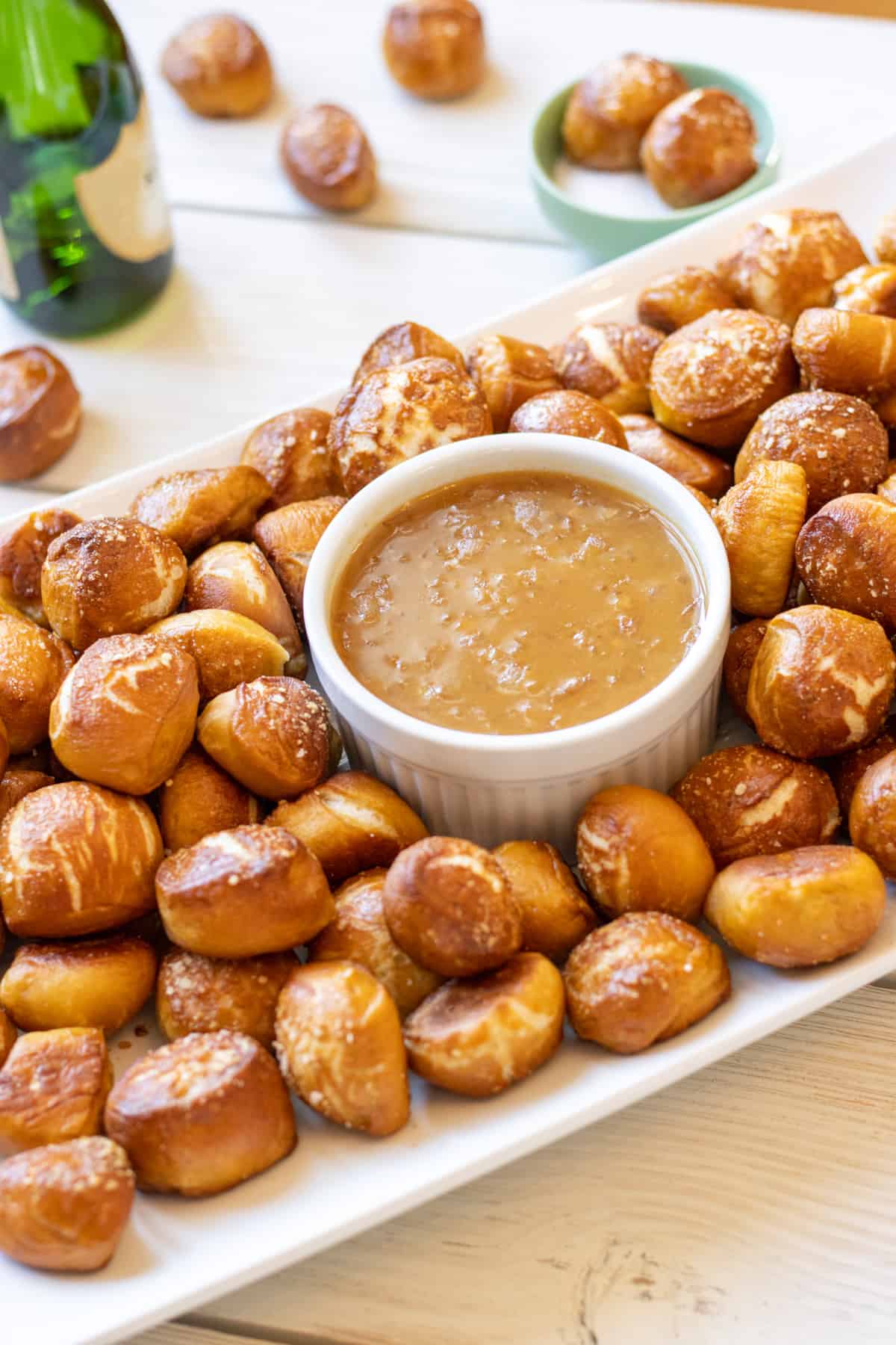 Pretzel bites on a platter with honey mustard dip and a green bottle in the background.