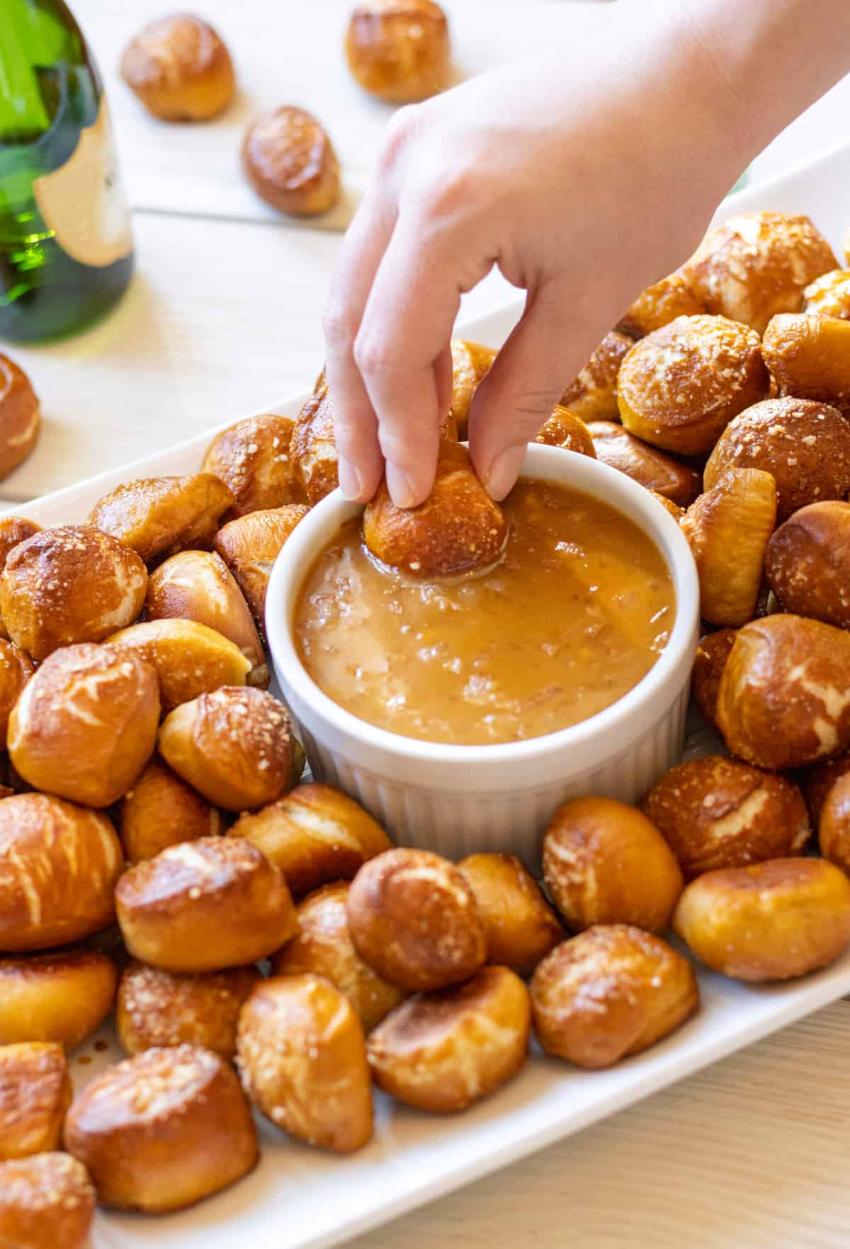 Pretzel bites on a tray with the honey mustard dip in a bowl with a hand dunking one of the pieces in the dip.