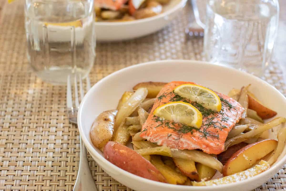 Salmon with lemon slices and dill in a plate with potatoes and fennel.