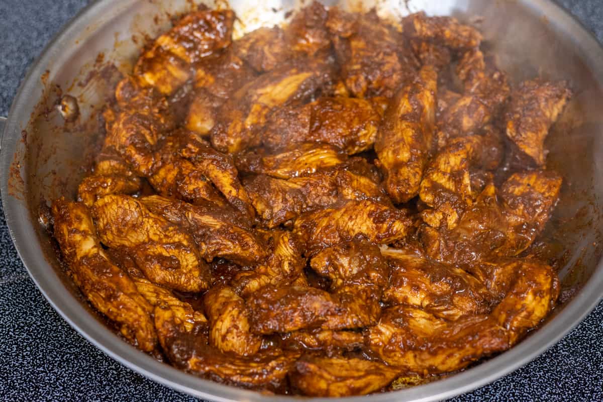 Chicken in an adobo sauce sautéing in a steel pan.