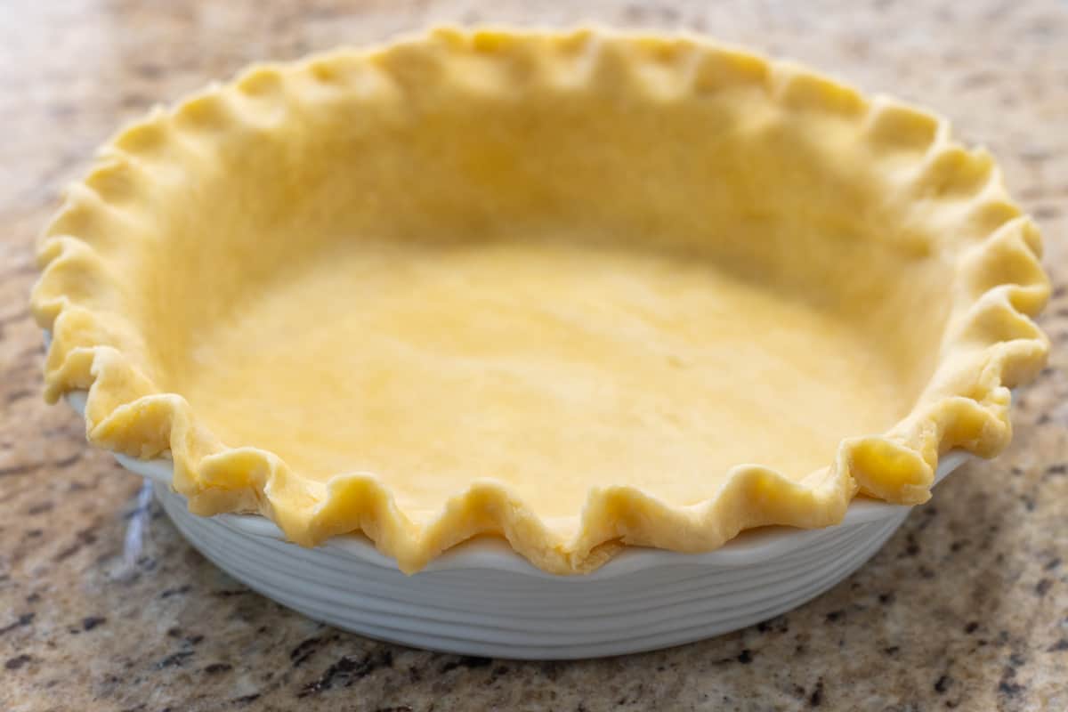 Raw pie dough with crimped edges in a pie plate.