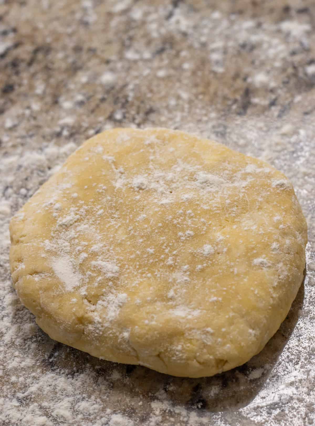 Disk of pie crust coated with flour on a counter.