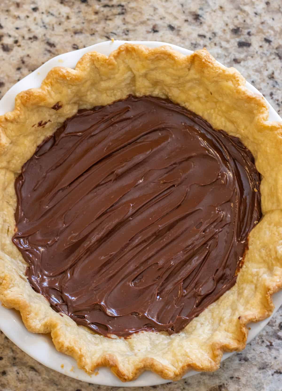 Chocolate ganache spread out in the bottom of a pie crust.