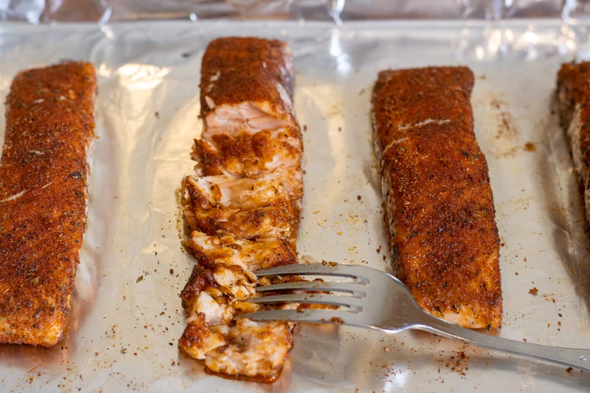 Salmon fillets on a foil-line baking sheet with one of them flaked apart.