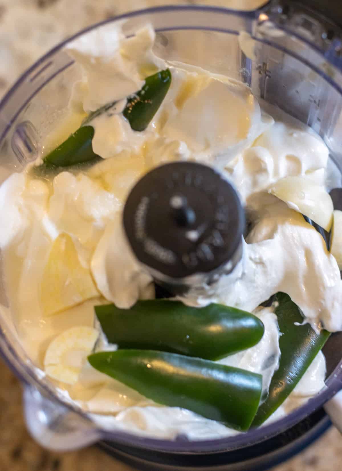 Sour cream, jalapeño, garlic clove, salt, and lime juice in a food processor ready to blend.