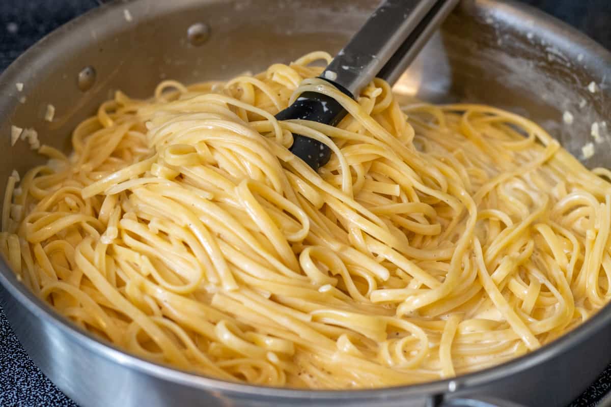 Linguine pasta tossed in the cream sauce with tongs in the steel pan.